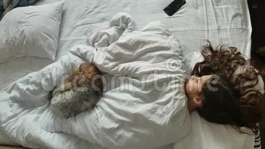 小可爱的女孩和睡在床上的毛茸茸的狗。 一个小女孩和一只睡得很香的小狗，一个浅黑色的小女孩睡着了